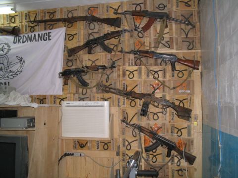 1981 Ford Bronco - Various firearms are displayed on a wall covered with wooden crates, alongside an "ORDNANCE" flag.