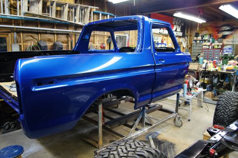 1979 Ford Bronco - A bright blue Ford Bronco body is undergoing restoration in a cluttered workshop.