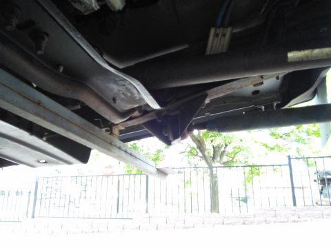 1996 Ford Bronco - This photo shows the undercarriage of a vehicle, including its frame and exhaust system, with a fence and trees in the background.