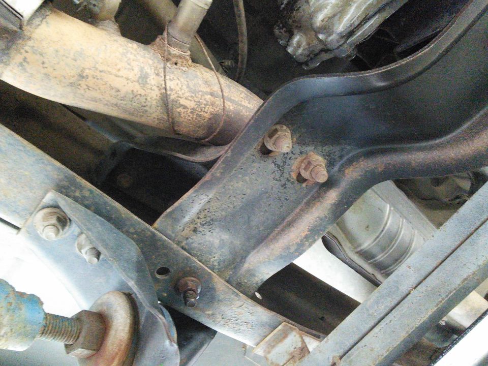 Undercarriage of a vehicle showing rusty exhaust pipe and metal brackets with bolts