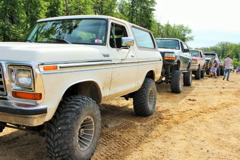 1979 Ford Bronco - A line of lifted off-road vehicles, including a white 1978 Ford Bronco, are parked on a dirt track.