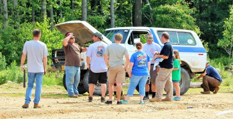 1979 Ford Bronco - People inspect a white SUV with its hood up in an outdoor setting.