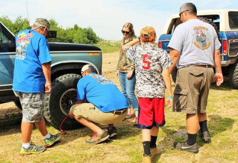 1979 Ford Bronco - Several people are attending to the tire of a classic Ford Bronco, with another Bronco visible in the background.