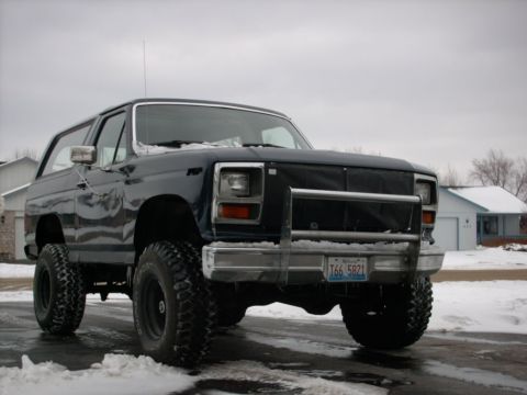 1986 Ford Bronco - This lifted 1986 Ford Bronco features a prominent brush guard and is seen parked in a snowy environment.