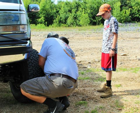 1979 Ford Bronco - A man works on changing a tire on a truck while a young boy observes the process.