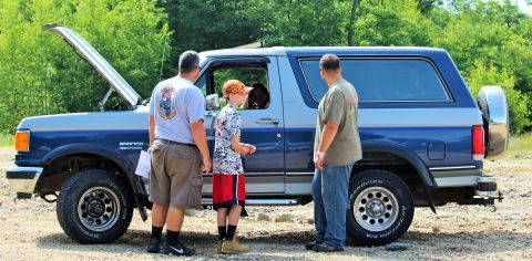 1979 Ford Bronco - Three people look at a blue and silver Ford Bronco with its hood open.