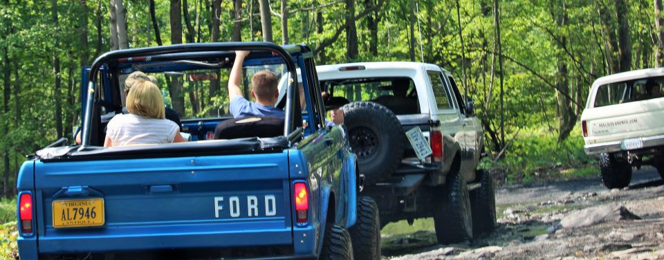 Blue 1979 Ford Bronco rear view with license plate AL7946, driving on a dirt road with two other Broncos