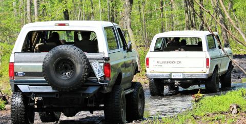 1979 Ford Bronco - Two Ford Broncos navigate a muddy path through a wooded area.