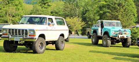 1979 Ford Bronco - Two modified Broncos are parked on a grassy field with trees in the background.