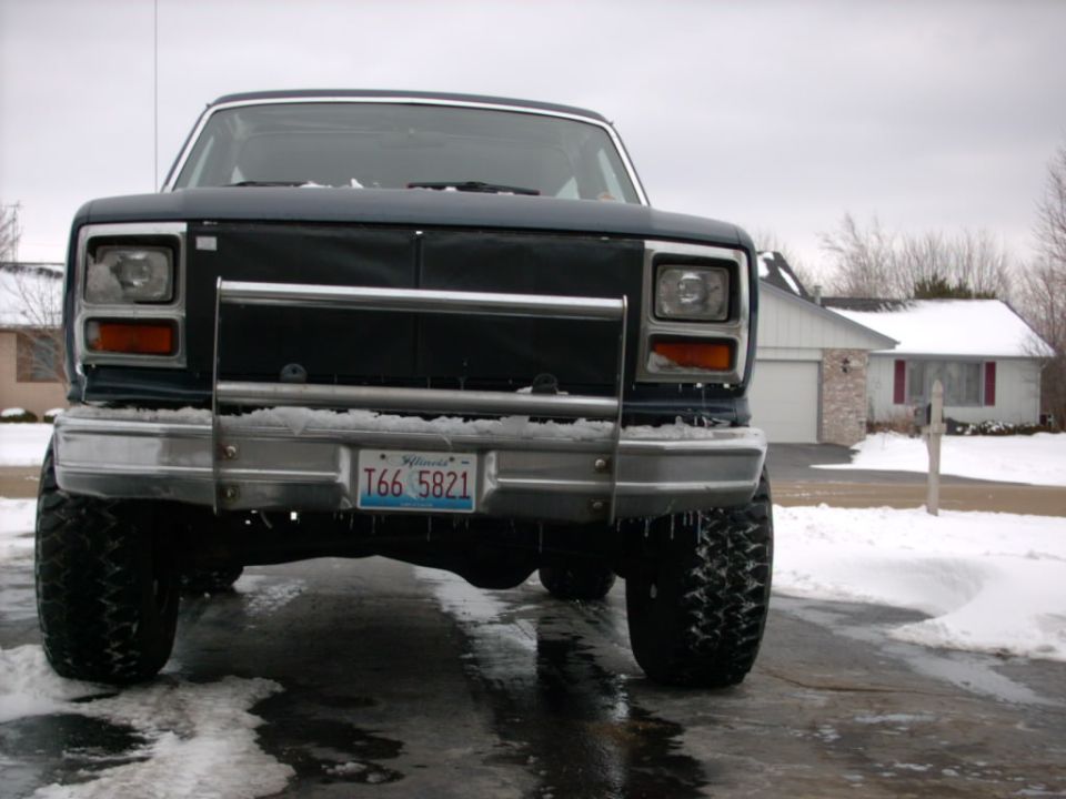 Dark lifted Ford truck, front view, on icy driveway with snow and house behind
