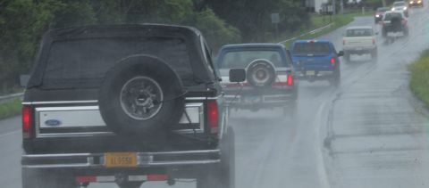 1979 Ford Bronco - Several vehicles, including a black Ford Bronco, drive down a wet road during a rainstorm.