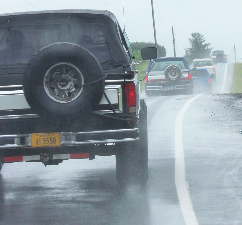 Rear view of a black Ford Bronco with a spare tire on the back, driving on a wet road behind other vehicles