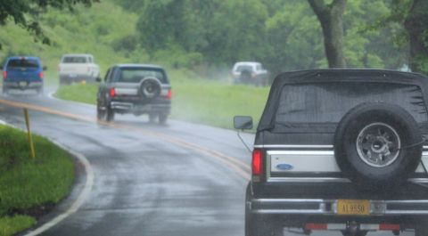 1979 Ford Bronco - Several vehicles drive on a wet road in the rain, including a black Ford Bronco.
