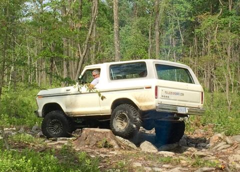 1979 Ford Bronco - White 1979 Ford Bronco tackles a challenging off-road trail with a driver behind the wheel.
