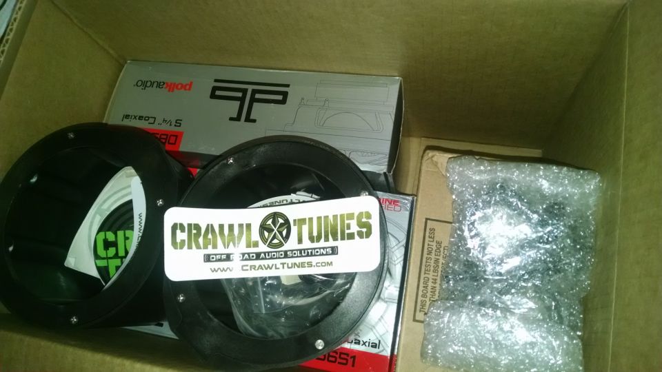 Two black car audio speakers and boxes with 'CrawlTunes' and 'Polk Audio' branding inside a cardboard box