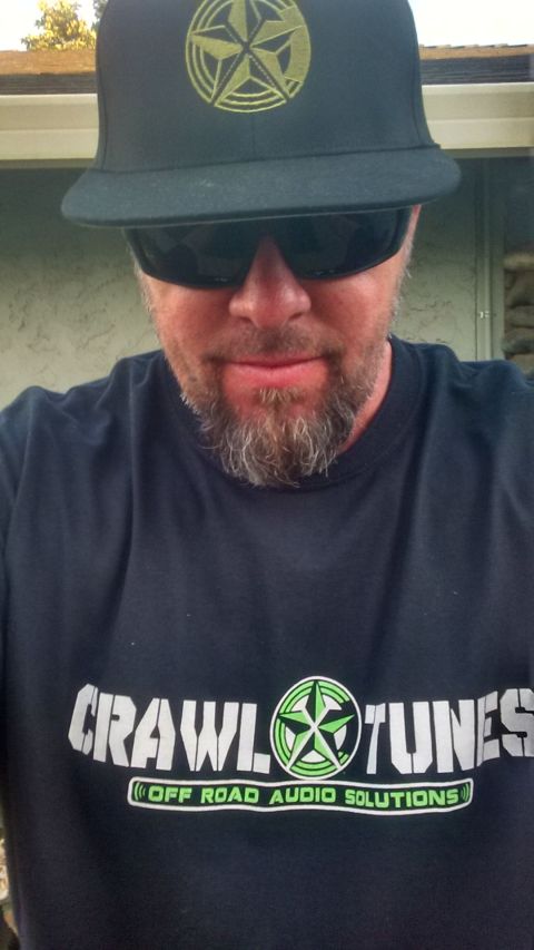 1985 Jeep CJ7 - Man wearing a t-shirt with "Crawl Tunes Off Road Audio Solutions" logo and a baseball cap with a star emblem.