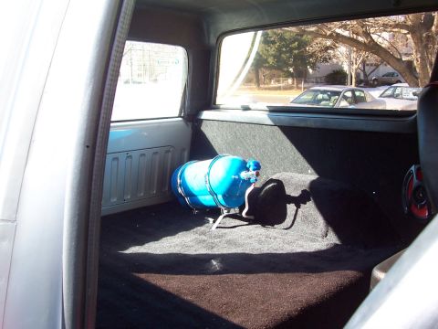 1990 Ford Bronco - The rear interior of a vehicle features a blue tank and a speaker, with other vehicles seen through the window.