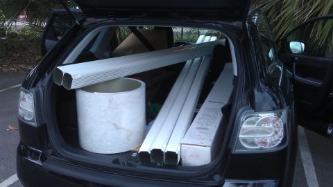 1994 Ford Bronco - A black SUV is shown with its trunk open, carrying various construction materials including long pipes and a large cylindrical item.