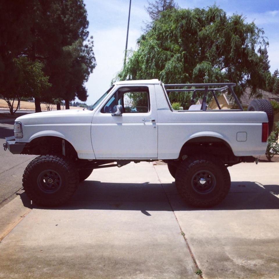 White SUV with lifted suspension and off-road tires parked on a sidewalk