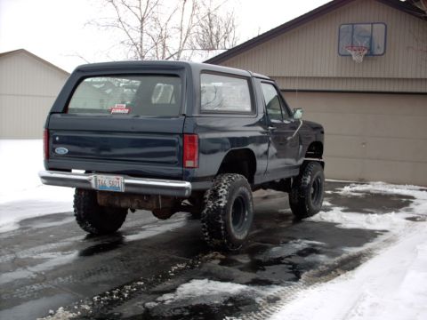 1986 Ford Bronco - Rear view of a dark blue SUV with lifted suspension and large tires parked in a snowy driveway.