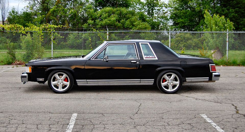 Black sedan with chrome trim and aftermarket wheels, seen from the side. Red brake calipers visible