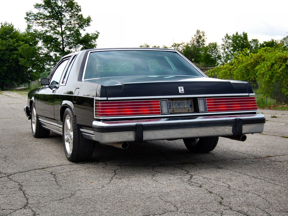 Rear of black 1980s Mercury Grand Marquis coupe with full-width taillights and dual exhaust.