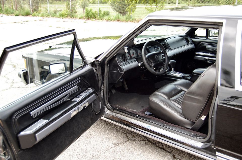 Black leather interior of a 1985 Mercury Grand Marquis, viewed from the passenger side with the door open