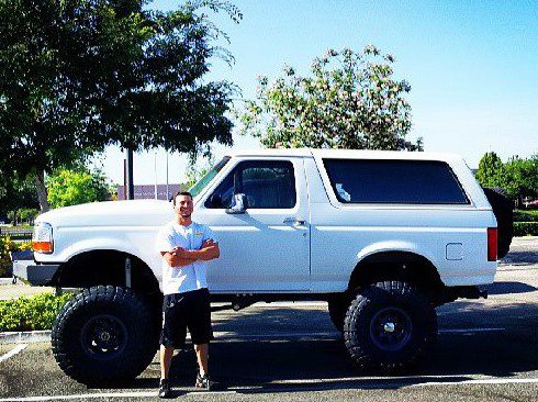 1995 Ford Bronco with lifted suspension and large tires parked outside with a man standing next to it