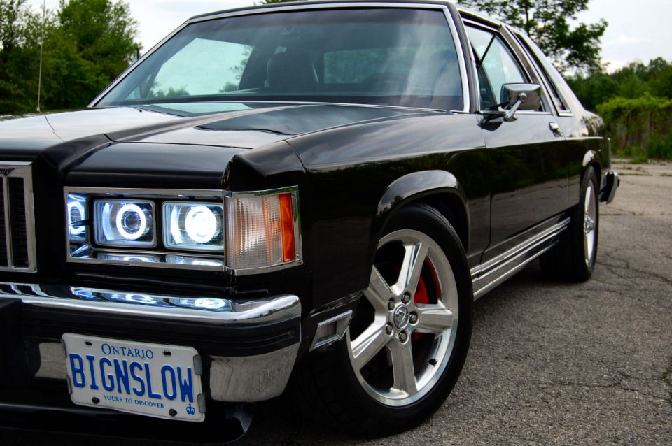 1985 Mercury Grand Marquis, black, with custom halo headlights and chrome wheels, parked on asphalt