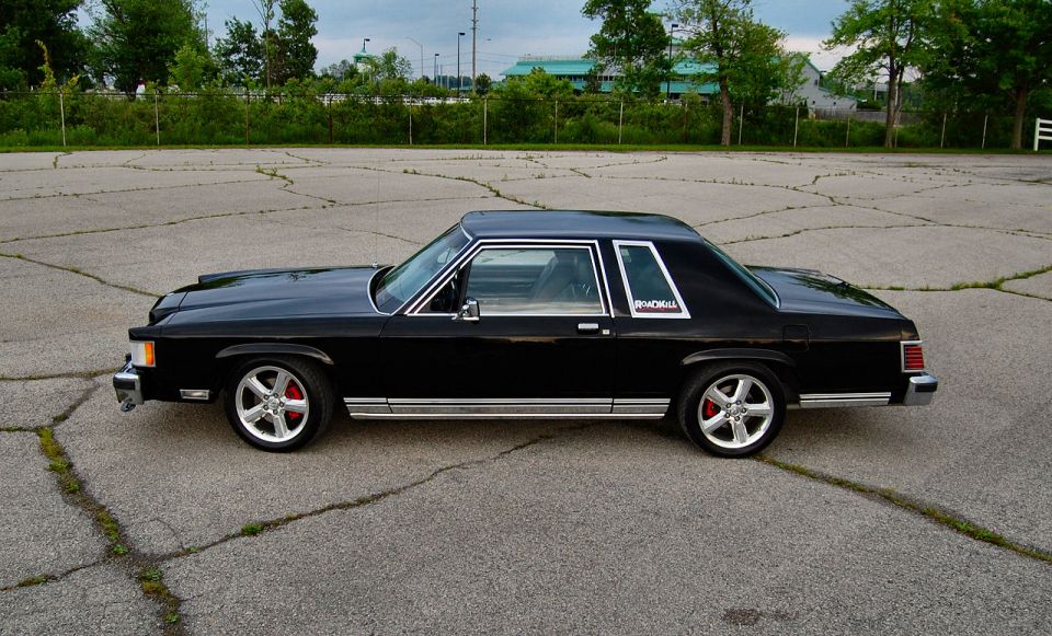 Black 1985 Mercury Grand Marquis coupe with chrome trim and red brake calipers, seen from the side