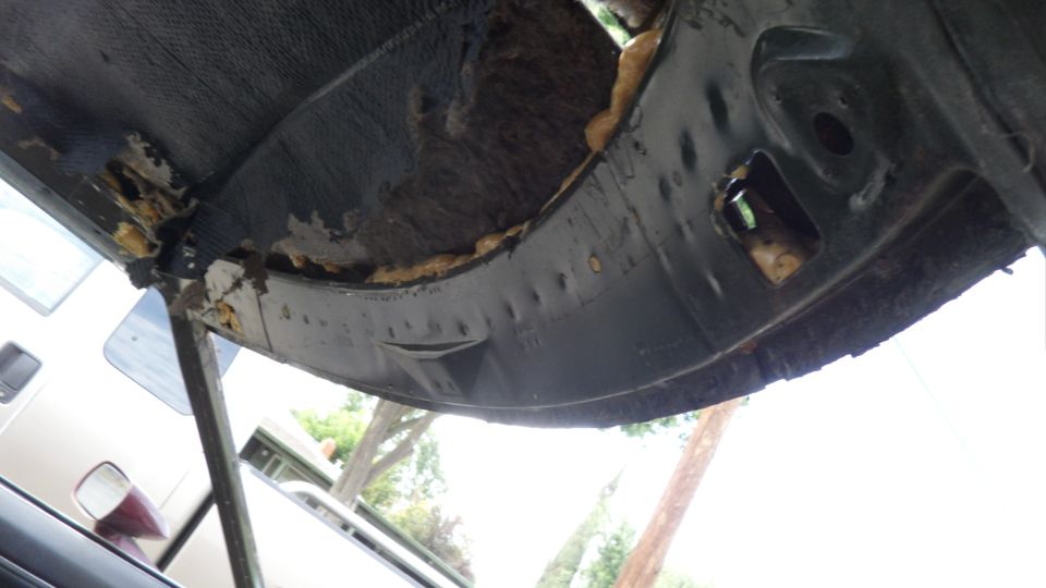 Underside of a car's body panel with insulation exposed and some rust