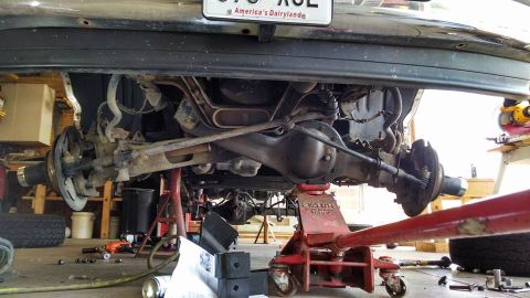 1994 Ford Bronco - Underside view of a vehicle's rear axle and suspension system being worked on in a garage.