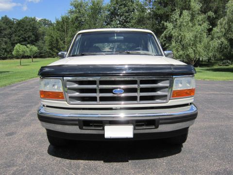 1994 Ford Bronco - This white Ford Bronco is parked outside on a paved driveway with trees in the background.
