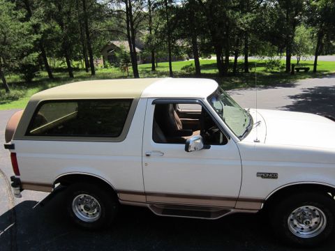 1994 Ford Bronco - A white 1994 Ford Bronco with a tan removable top is parked outdoors.
