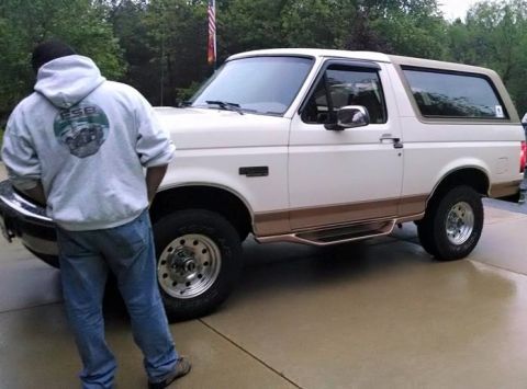 1994 Ford Bronco - A man stands beside a white Ford Bronco with brown trim and running boards.