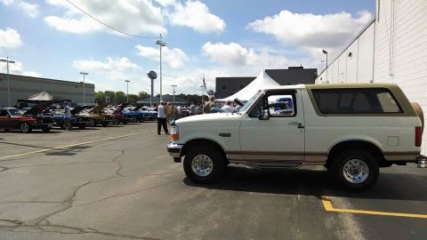 1994 Ford Bronco - A white Ford Bronco with tan trim is parked at an outdoor car show with other vehicles in the background.
