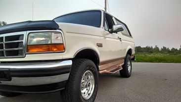 1994 Ford Bronco - This 1994 Ford Bronco is shown from a low angle, parked on the shoulder of a road with trees in the background.