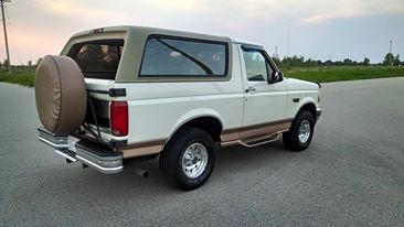1994 Ford Bronco - This 1994 Ford Bronco is shown from the rear quarter angle, parked on a road with a tan top and spare tire mounted on the rear.