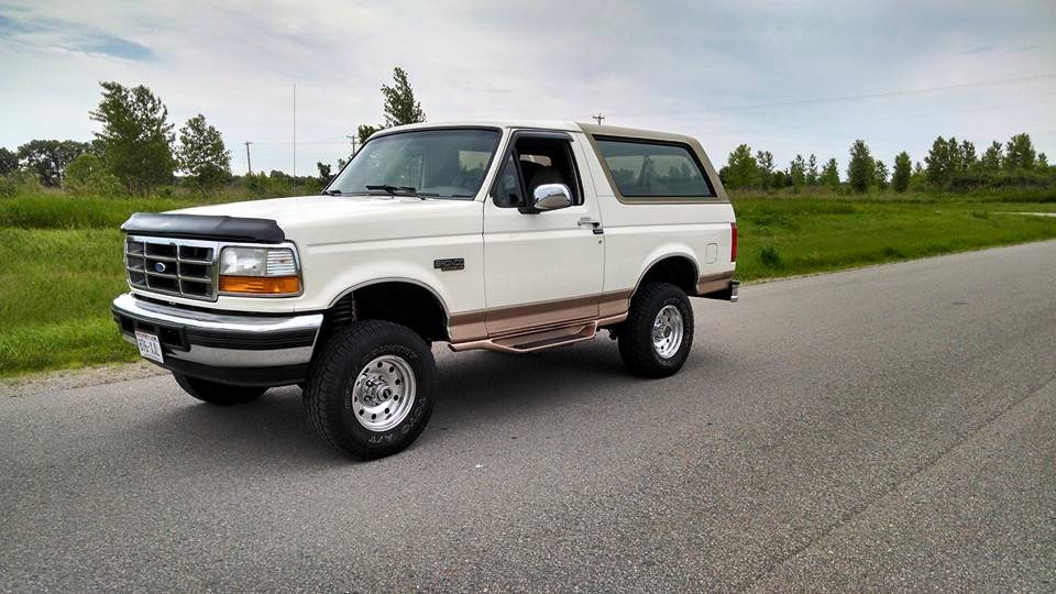 White Ford Bronco with brown trim and aftermarket wheels parked on asphalt road