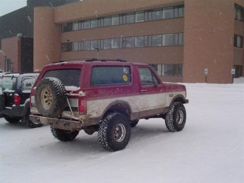 1994 Ford Bronco - A two-tone Ford Bronco sits in a snowy lot outside a brick building.
