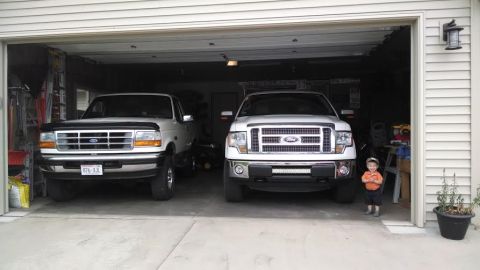 1994 Ford Bronco - Two Ford trucks, a 1994 Bronco and a newer F-150, parked side-by-side in a garage.