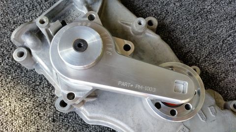 2003 Ford Crown Victoria - machined aluminum engine timing cover with a polished tensioner arm, stamped PART# PM-1003, rests on grey carpet.