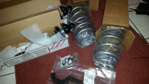 2003 Ford Crown Victoria - Two grey coil springs, shock or control-arm components and bagged hardware sit on red carpet beside their boxes.