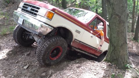 1979 Ford Bronco - A lifted Ford Bronco is shown navigating a steep, wooded trail with large tires.