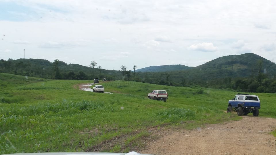Blue and white 1979 Ford Bronco rear view on dirt road with other vehicles