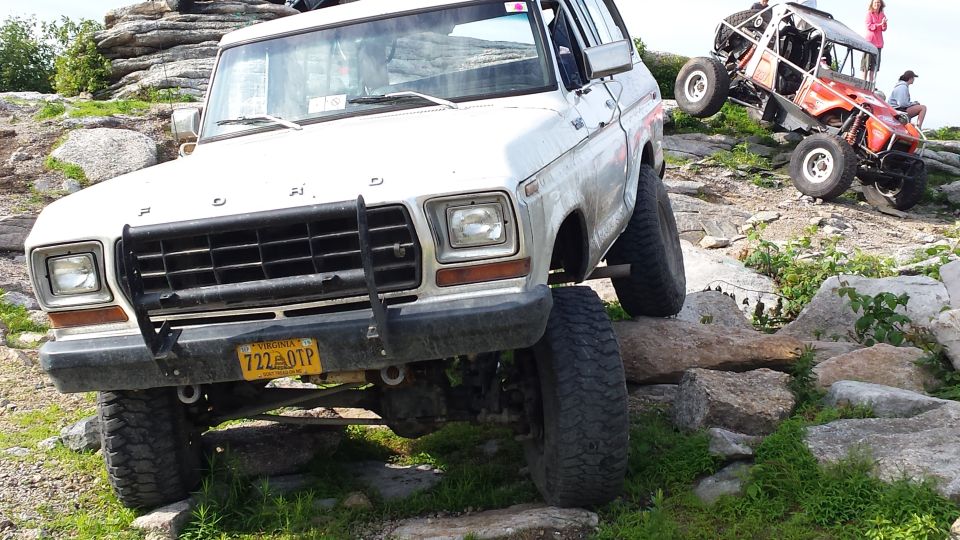 White Ford Bronco with lifted suspension on rocks; orange off-road buggy in background