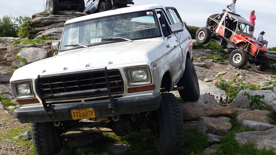 White 1979 Ford Bronco climbing rocks with another off-road vehicle behind it