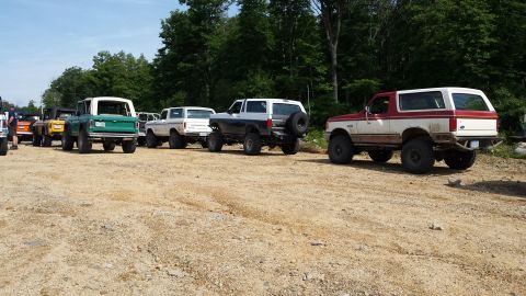 1979 Ford Bronco - A line of off-road SUVs, including a red and white 1979 Ford Bronco, parked on a dirt lot.