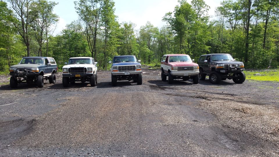 Five lifted Ford Broncos parked in a dirt lot with trees in the background