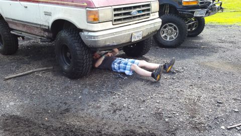 1979 Ford Bronco - A person works on the underside of a lifted Ford truck, with another similar vehicle parked nearby.